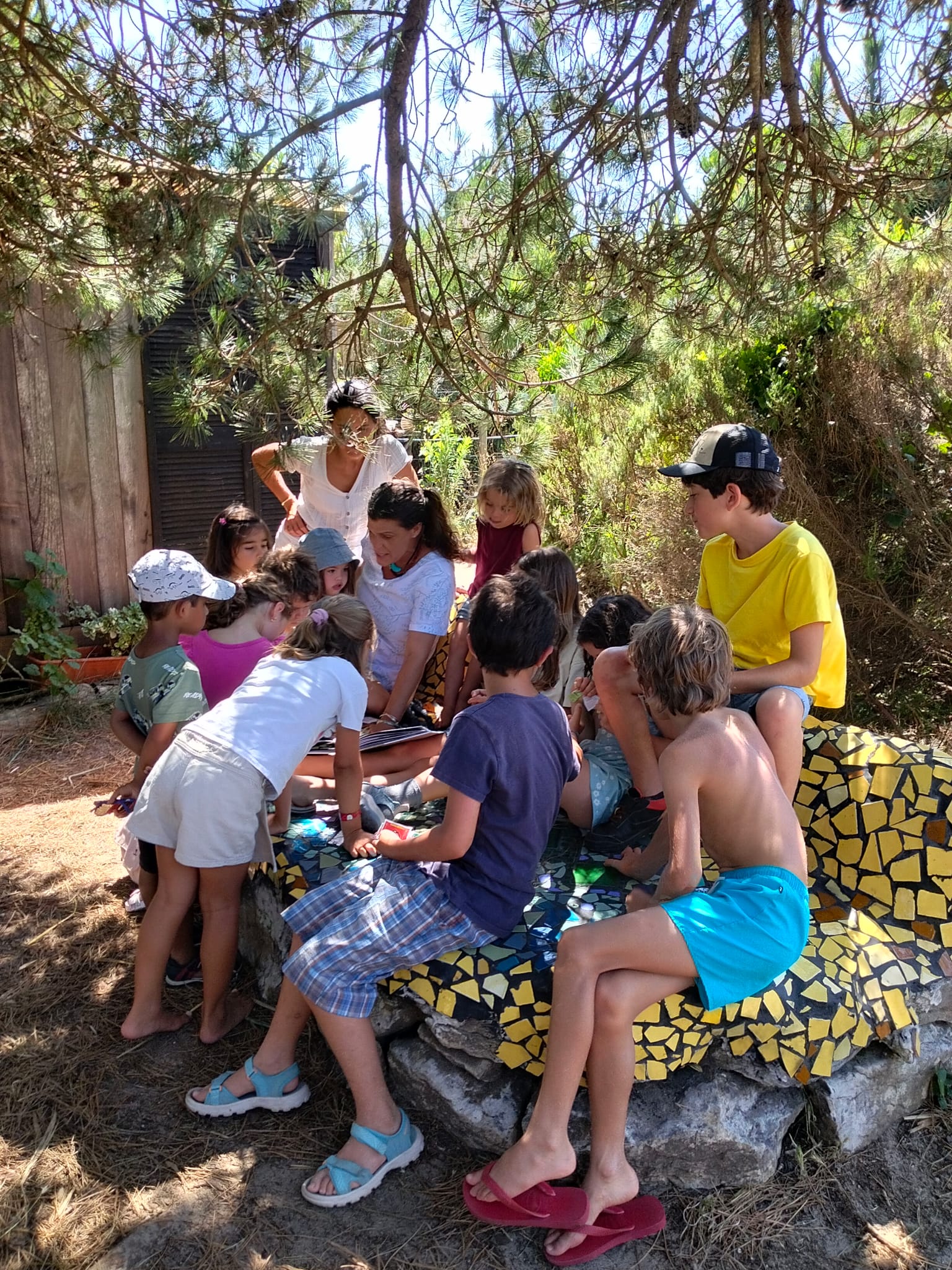 Crianças reunidas à volta de um livro com uma educadora, no banco de mosaico